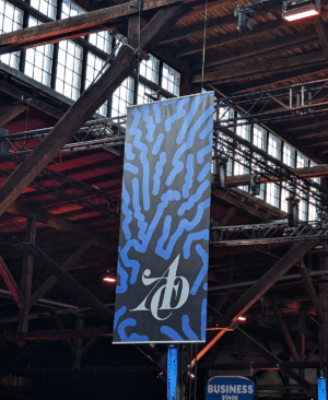 Großes vertikales Banner mit blau-schwarzem Muster und ADC-Logo hängt in einer Industriehalle.